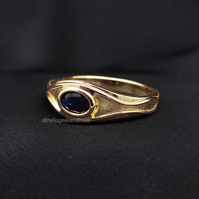 Anillo dorado con montura ondulada y piedra azul oscura oval