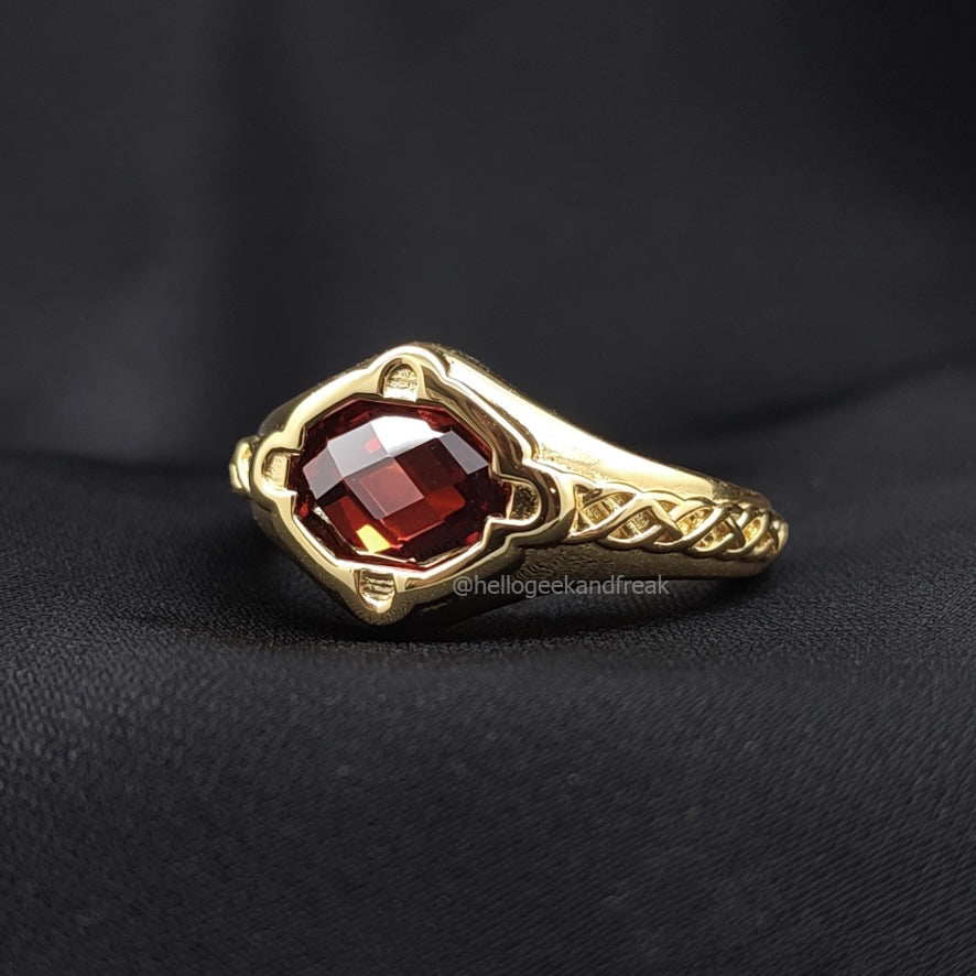 Anillo dorado con piedra rectangular roja oscura y marco con detalles calados.