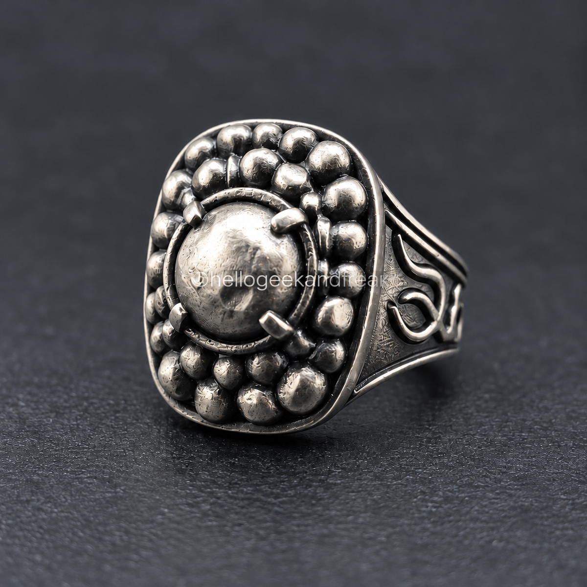 Anillo de metal plateado con relieve de roca y dibujo circular en la cara