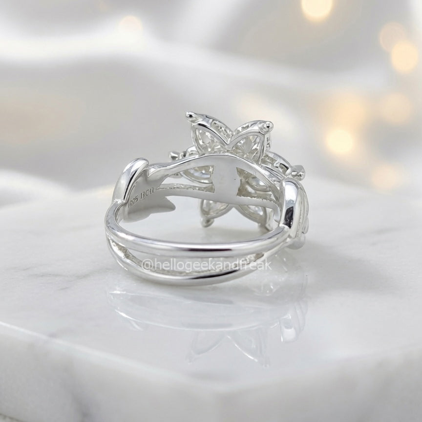 Anillo plateado con flor central; vista lateral de la montura abierta