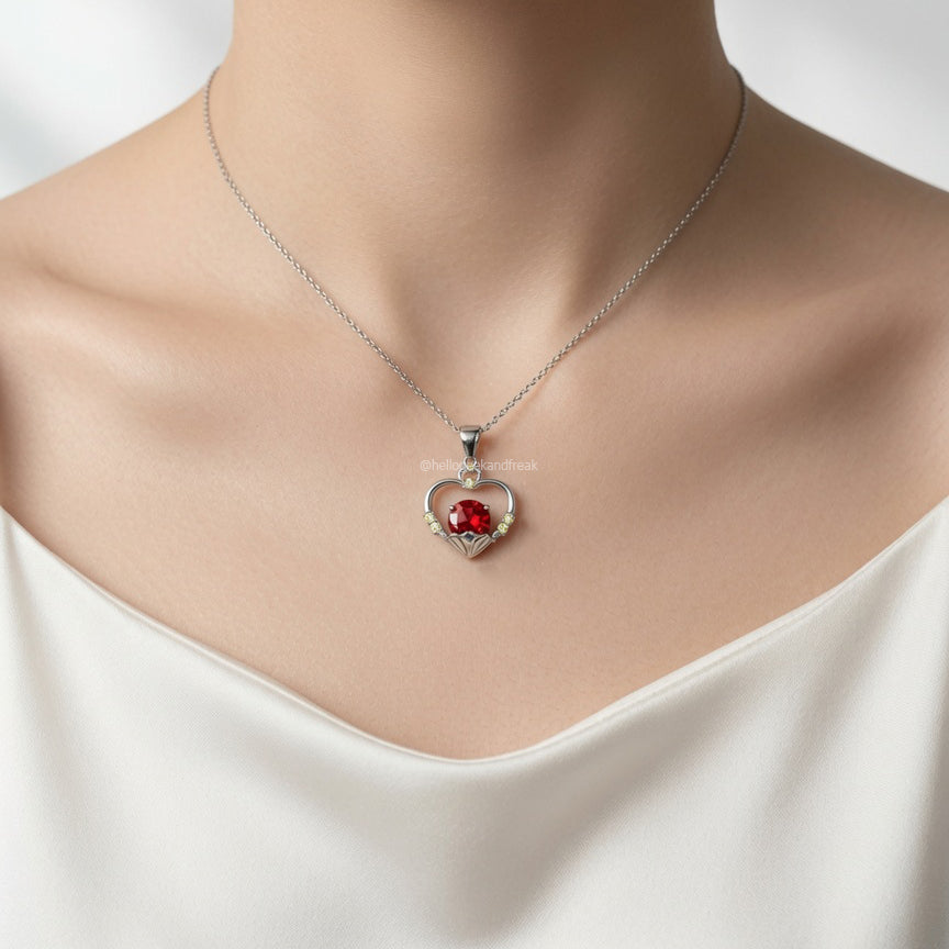 Collar con colgante corazón plateado con piedra roja y detalles brillantes.