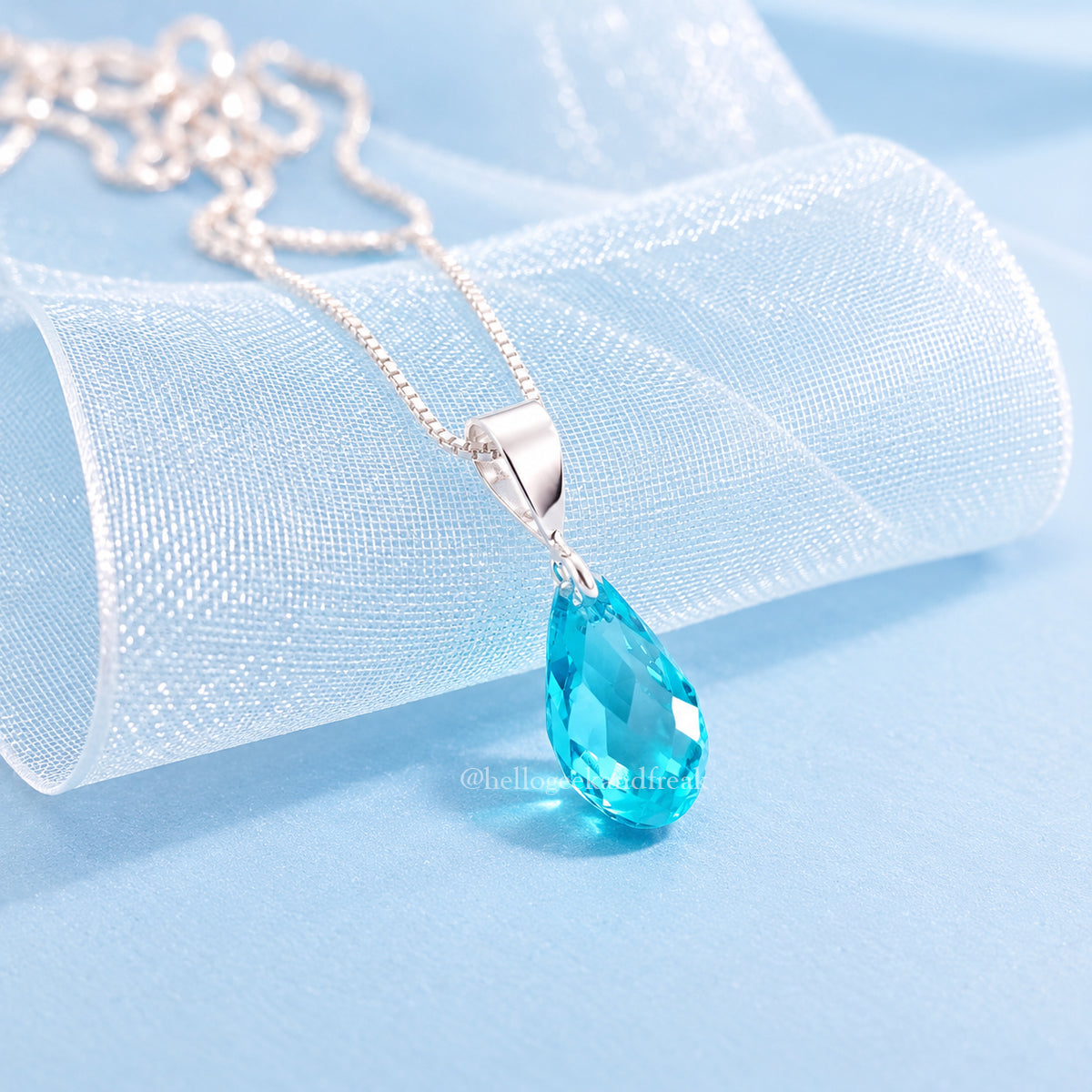 Colgante de plata con cristal azul gota, sobre tela de organza azul